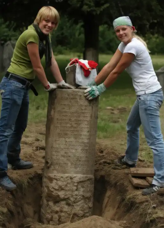 Deux jeunes debout de chaque côté d'un puits creusé dans le sol.