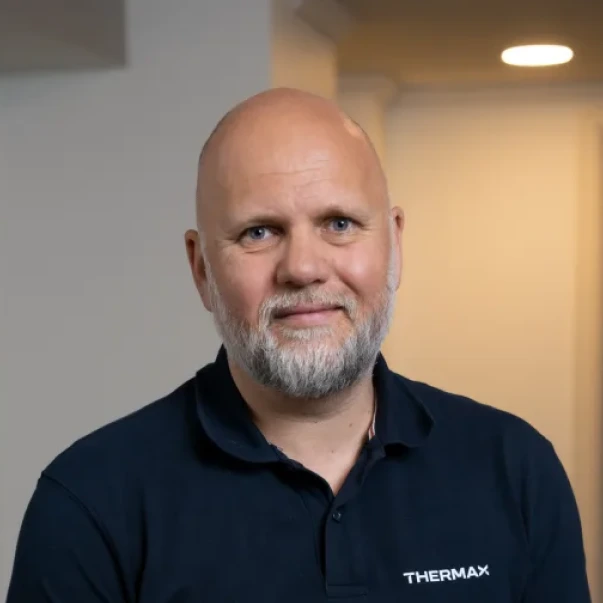 Portrett av en smilende, skallet mann med grått skjegg iført mørk blå Thermax-polo.