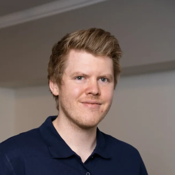 Portrett av en mann med lyst hår som smiler svakt og har på seg en mørk blå skjorte.