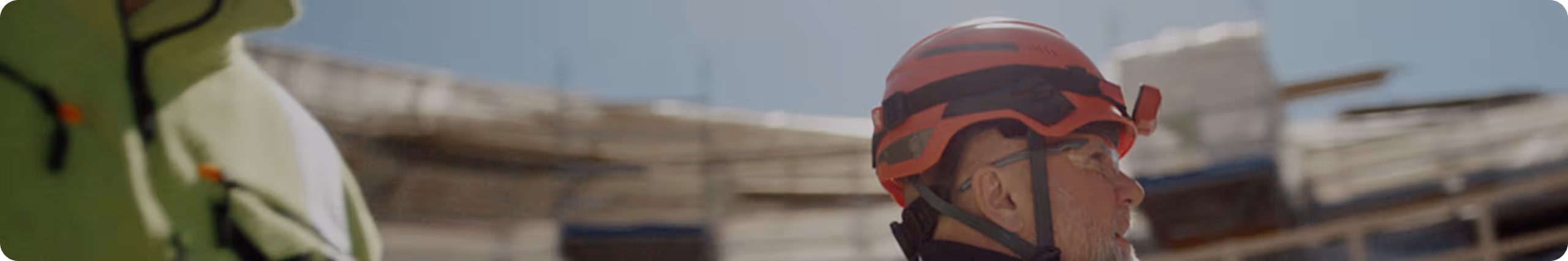 Nærbilde av en mann med rødt vernehjelm og vernebriller på en byggeplass.