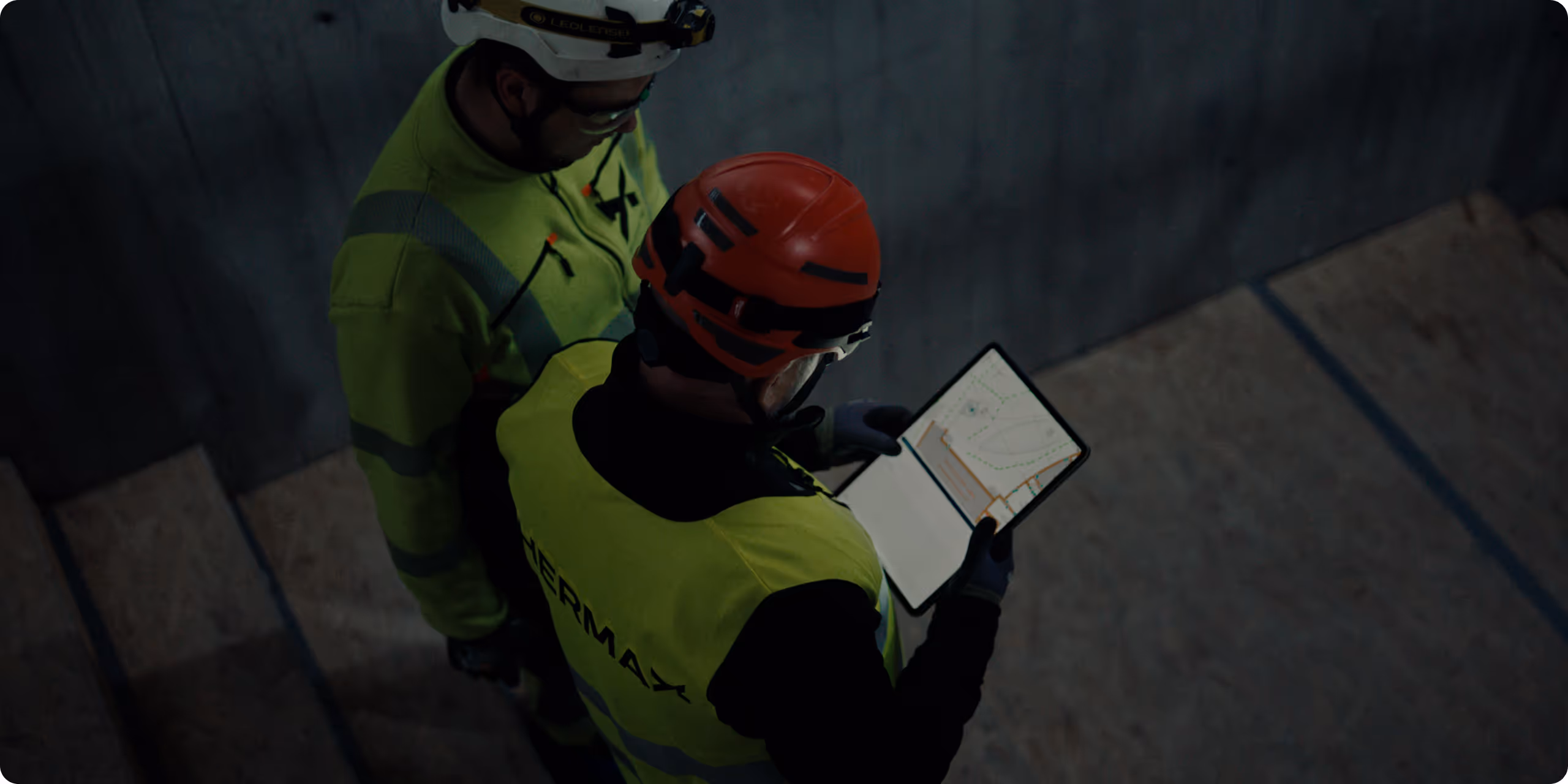 To arbeidere i verneutstyr og hjelmer ser på en digital nettbrett med et teknisk kart.