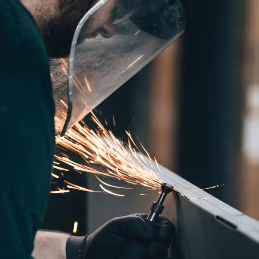 Person som bruker vernebriller og ansiktsskjerm mens de sliper metall og skaper gnister.