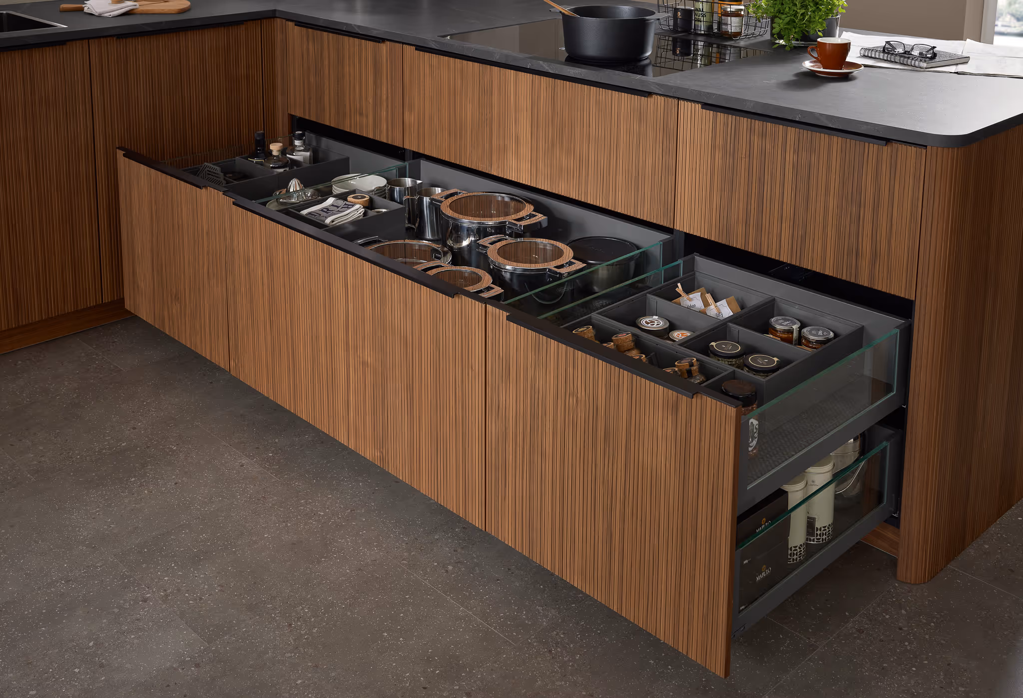 Offene Küchenschubladen mit organisierten Töpfen, Gewürzen und Küchenutensilien in einer modernen Holzküche mit dunkler Arbeitsplatte.