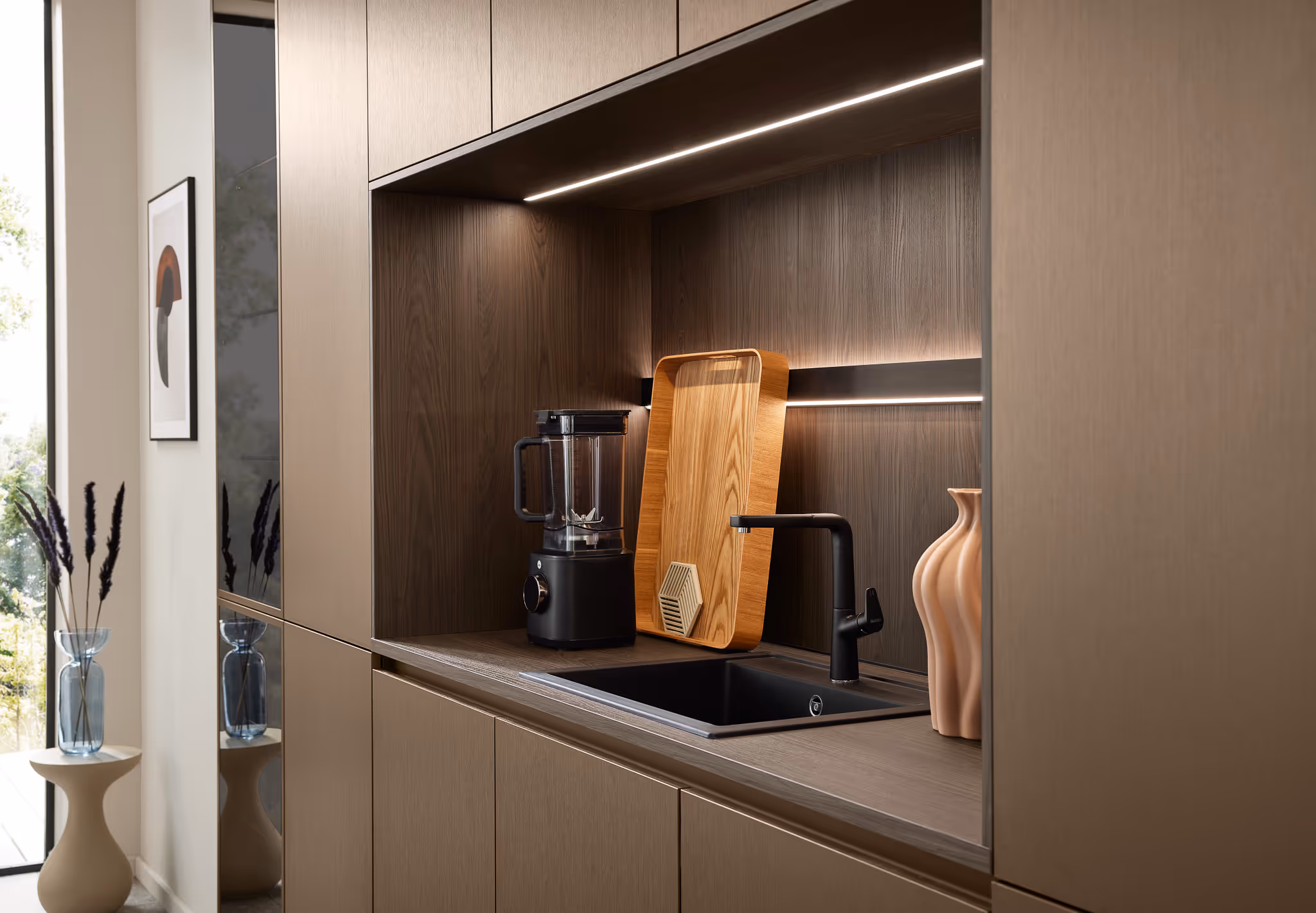 Moderne Küche mit eingebauter Spüle, schwarzem Wasserhahn, Holzschneidebrett, schwarzem Standmixer und dekorativer Vase.