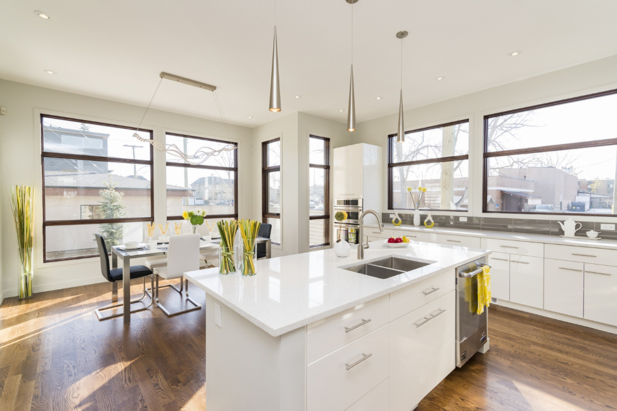 Bright modern kitchen with white cabinets, an island with a sink, and large windows letting in natural light.