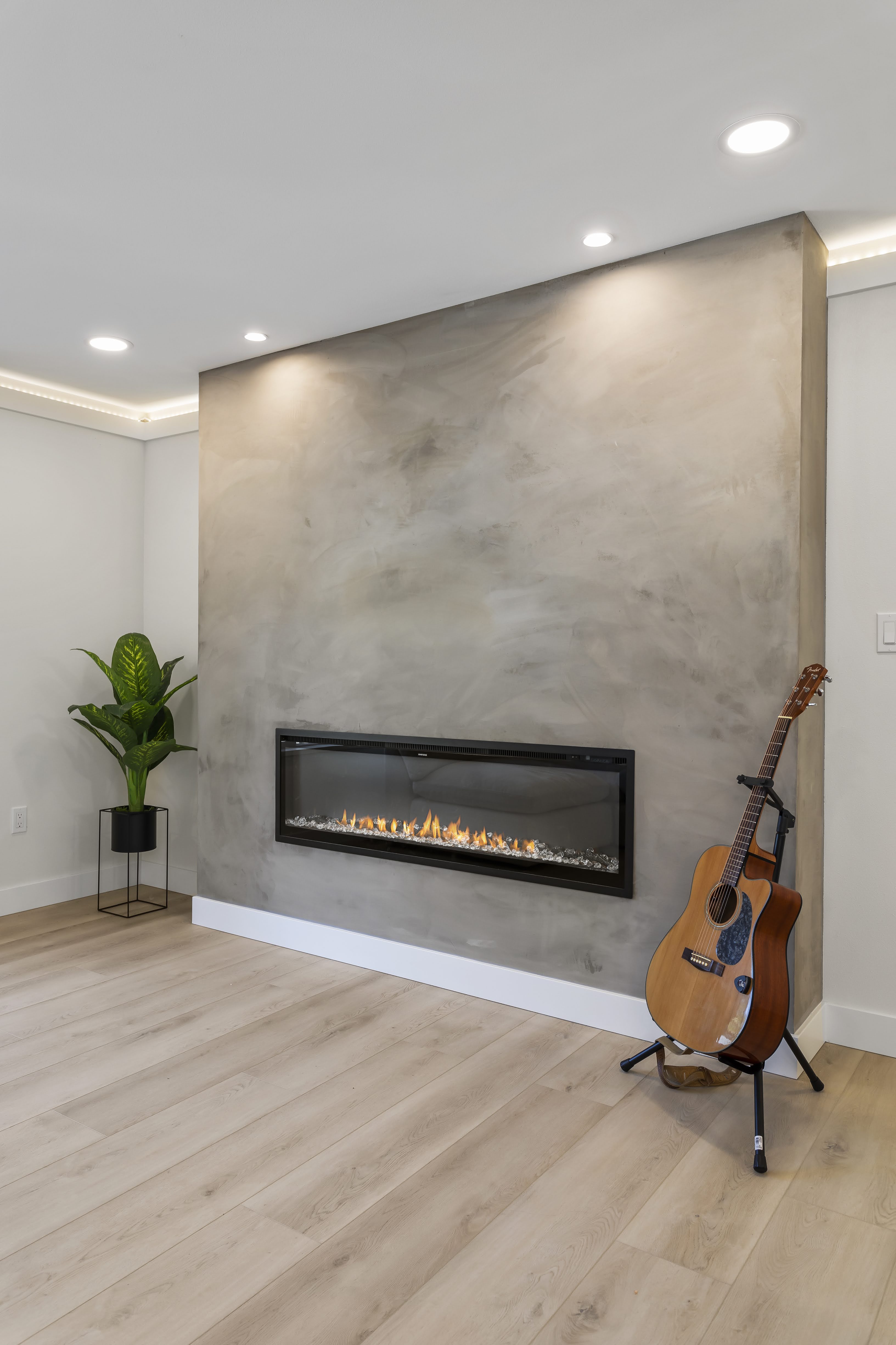 Modern living room with a linear fireplace set in a textured wall, light wood flooring, recessed lighting, and a guitar on a stand