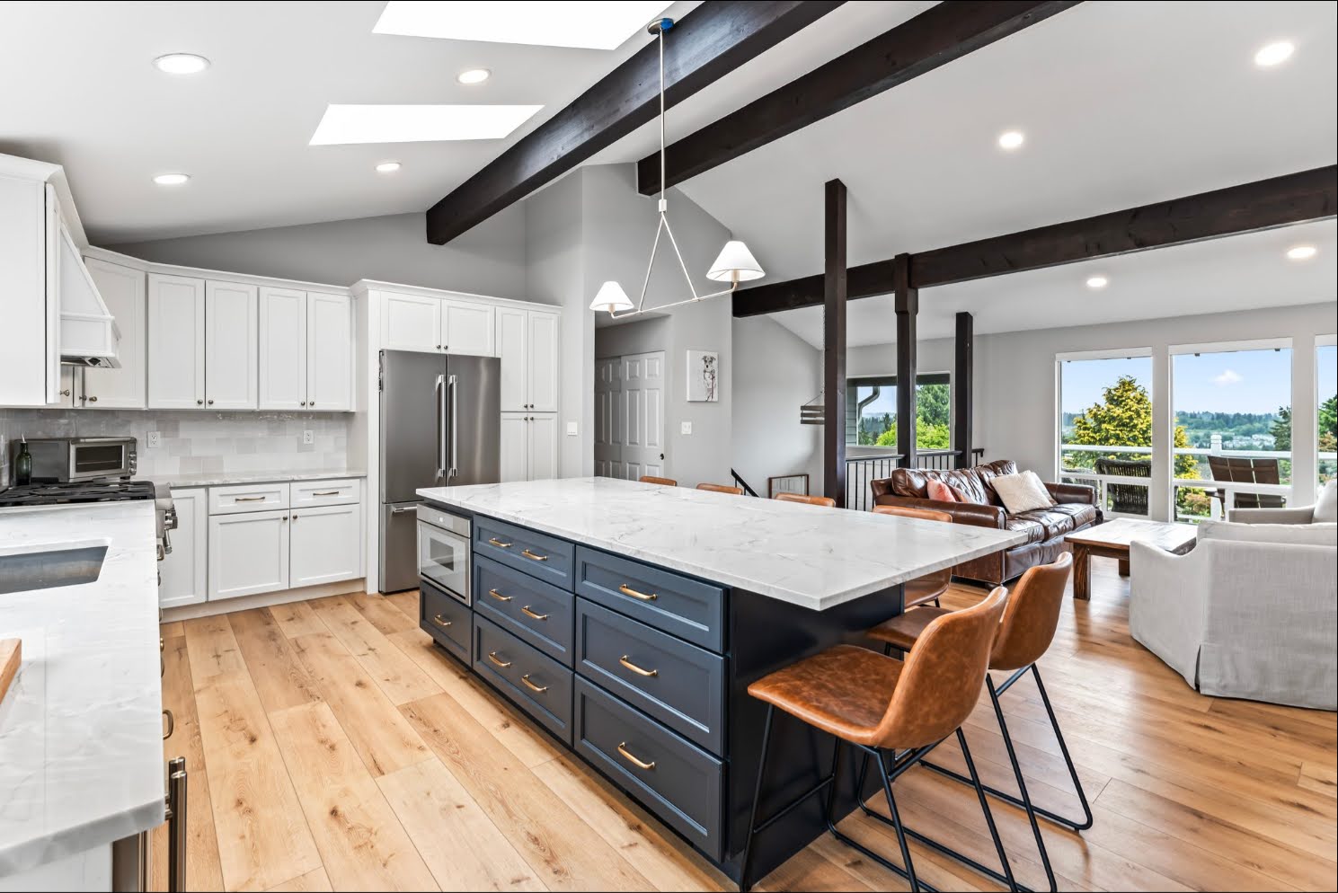 Open kitchen with navy island and white cabinets leading into a bright living room with large windows