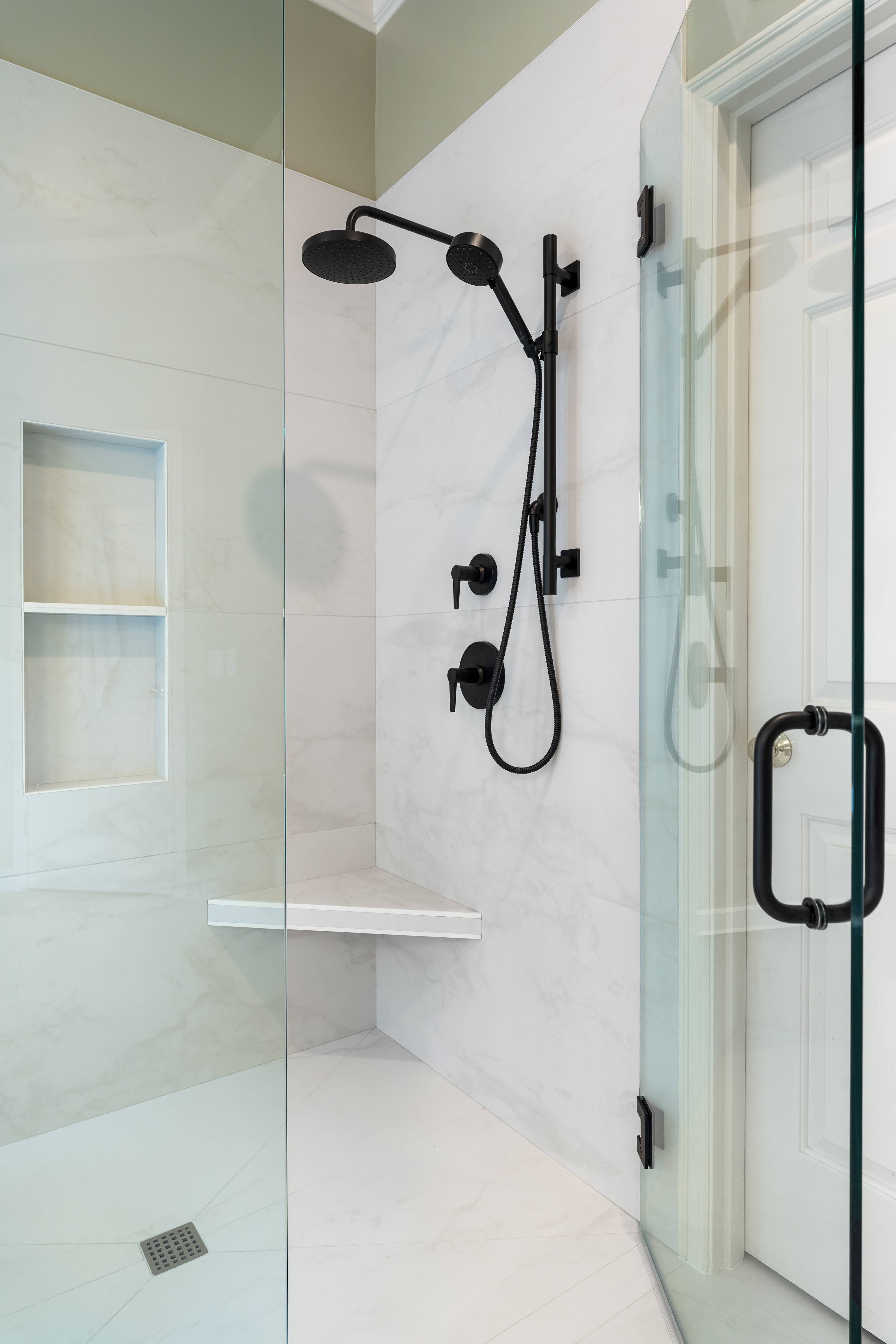 Sleek shower design with black rainfall fixtures, corner bench, recessed storage niche, and frameless glass door