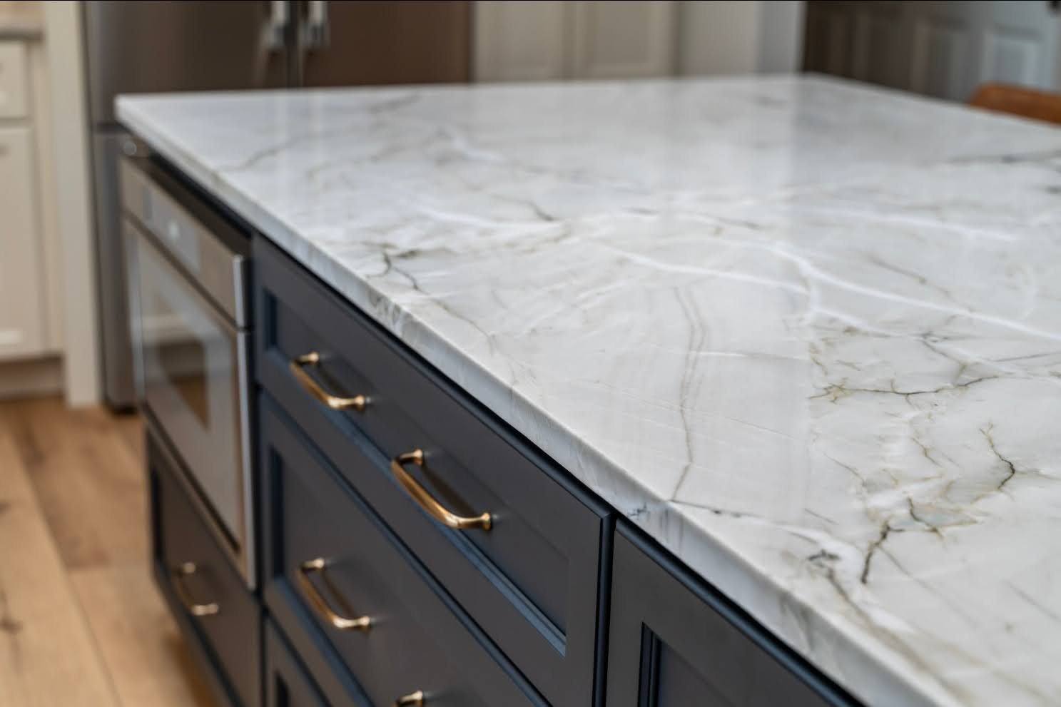 Close-up of a marble-look kitchen island countertop with navy cabinets and gold hardware in a modern remodeled kitchen