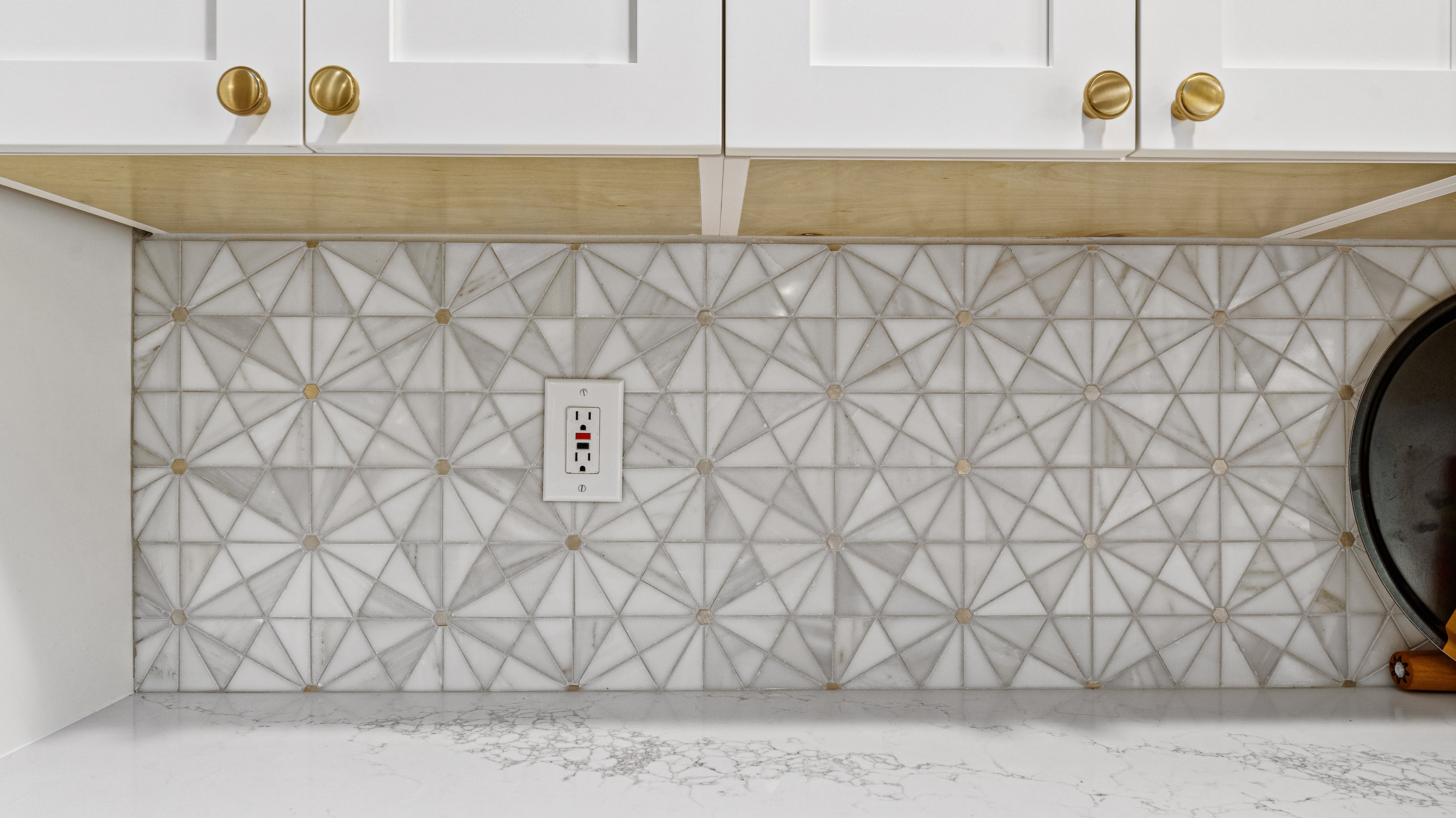 Close-up of a modern kitchen backsplash featuring geometric marble tiles and white cabinetry
