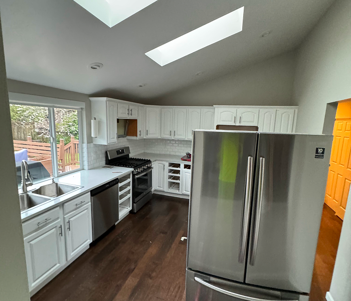 Dark, outdated kitchen with white cabinets, old flooring