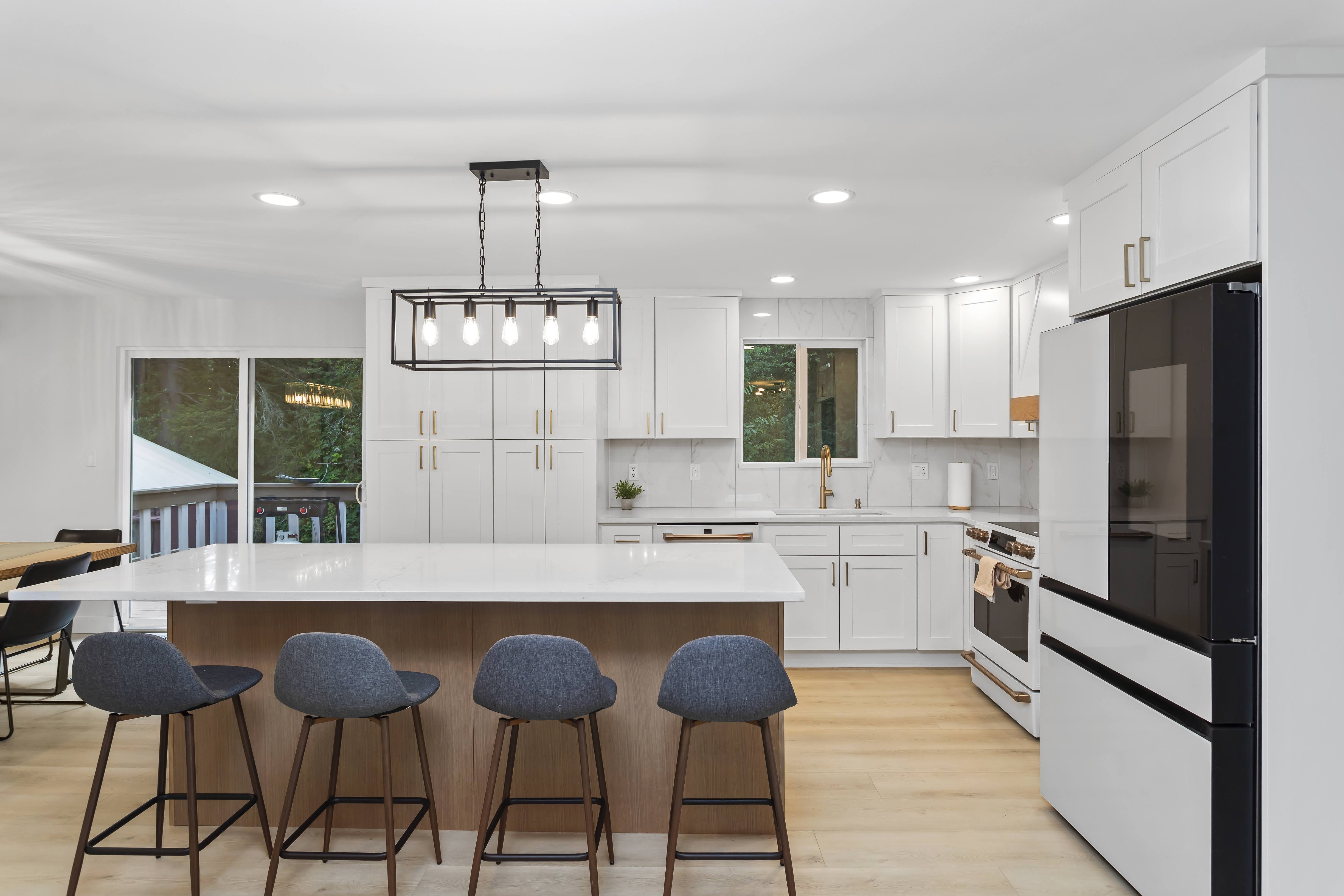 Bright modern kitchen with white cabinets, large island, gold fixtures, wood floors, and contemporary lighting, remodeled in an open-concept layout