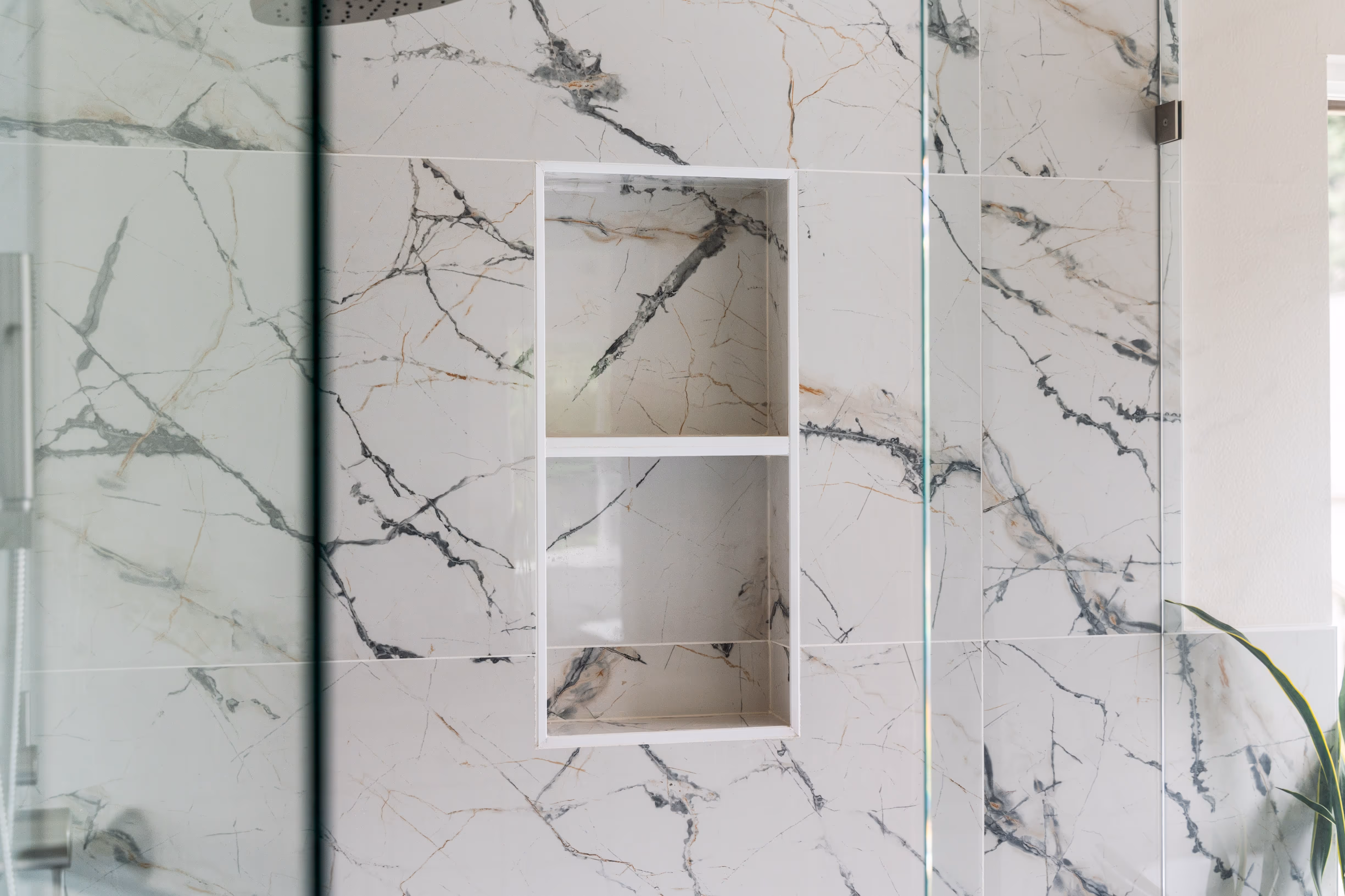 Close-up of a built-in shower niche set in large marble-pattern tiles inside a modern walk-in shower