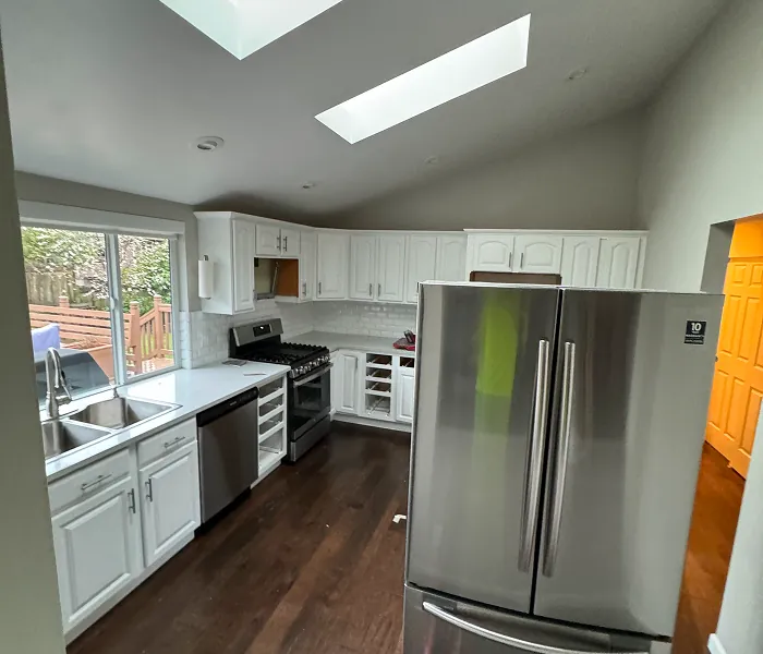 Dark, outdated kitchen with white cabinets, old flooring