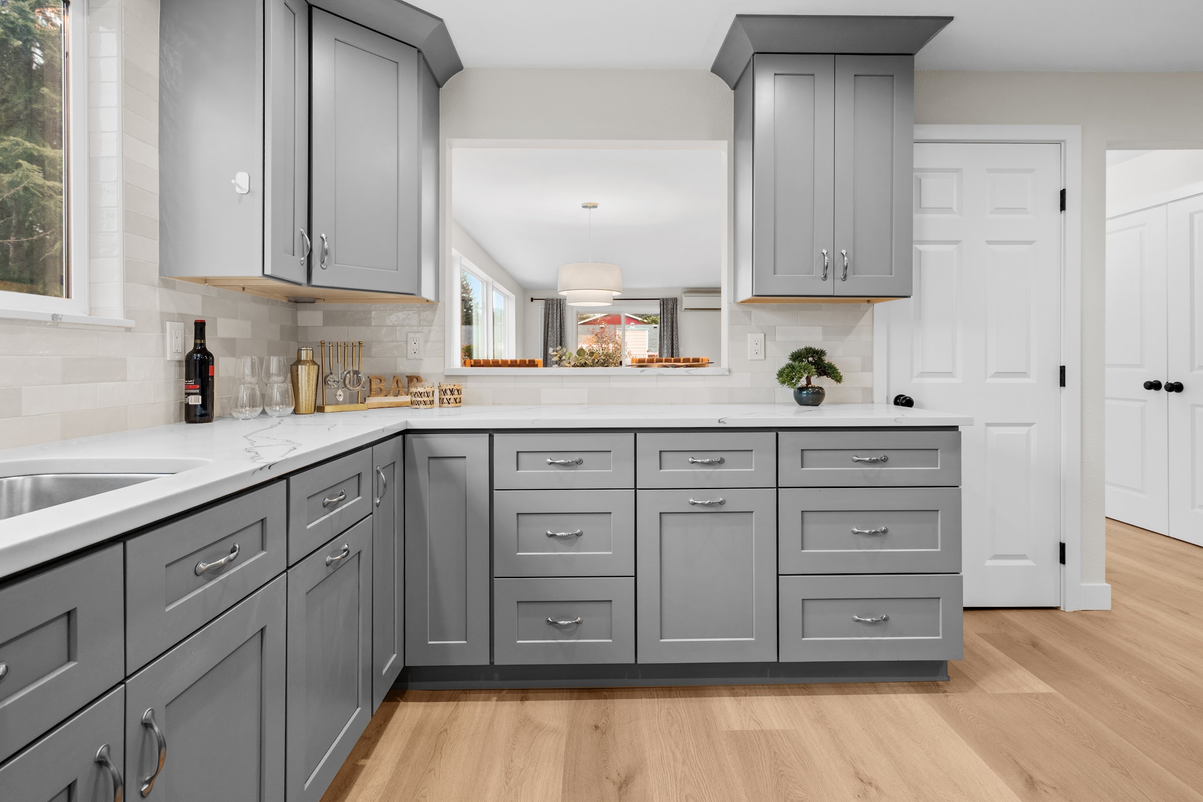 Gray shaker cabinet kitchen with cream stacked tile backsplash, white quartz countertops, bar area with wine glasses, and pass-through window, Crafthaus kitchen remodel