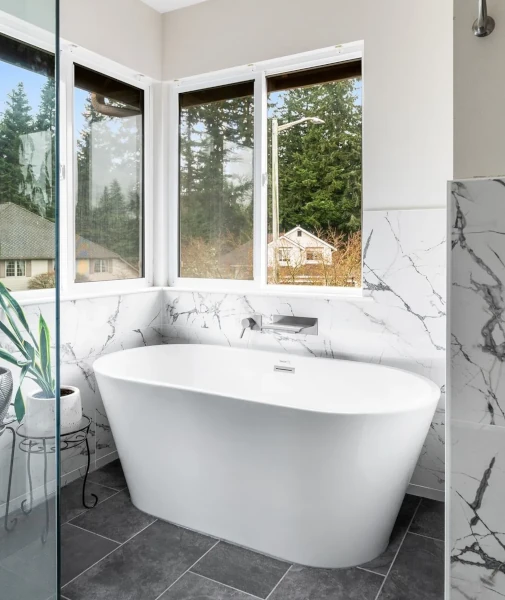 Bright bathroom corner featuring a freestanding white tub, marble wall tile
