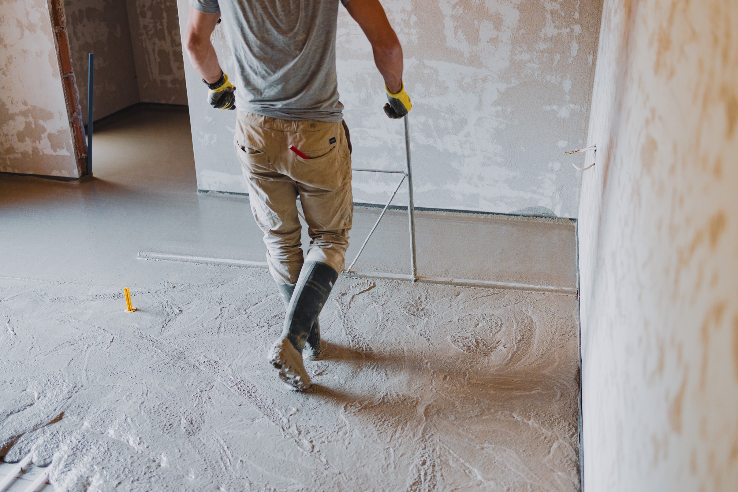 Construction worker wearing gloves and rubber boots leveling freshly poured concrete on a floor