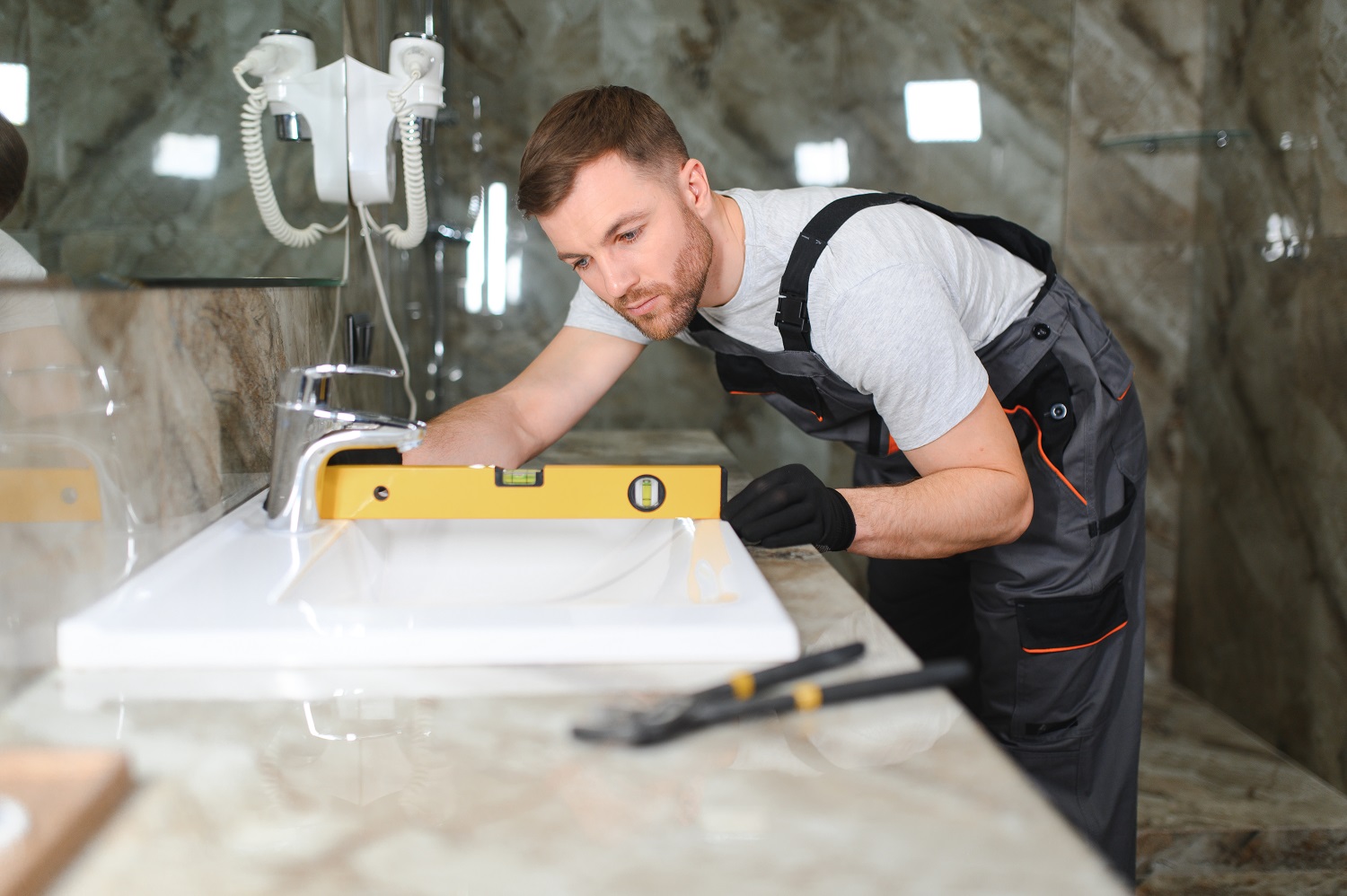 Contractor using a level to install a white bathroom sink on marble countertop during a bathroom renovation