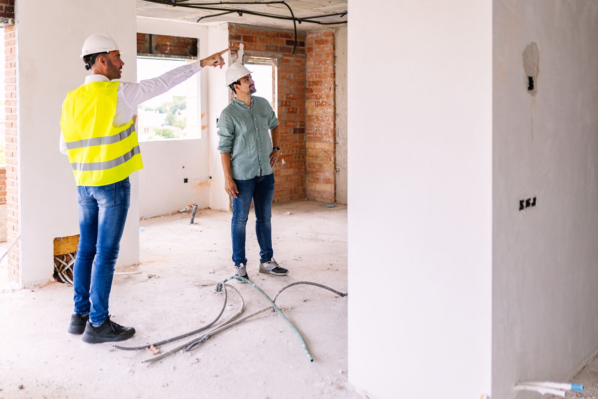 Engineer and homeowner discussing cost of renovation vs new construction inside an unfinished building