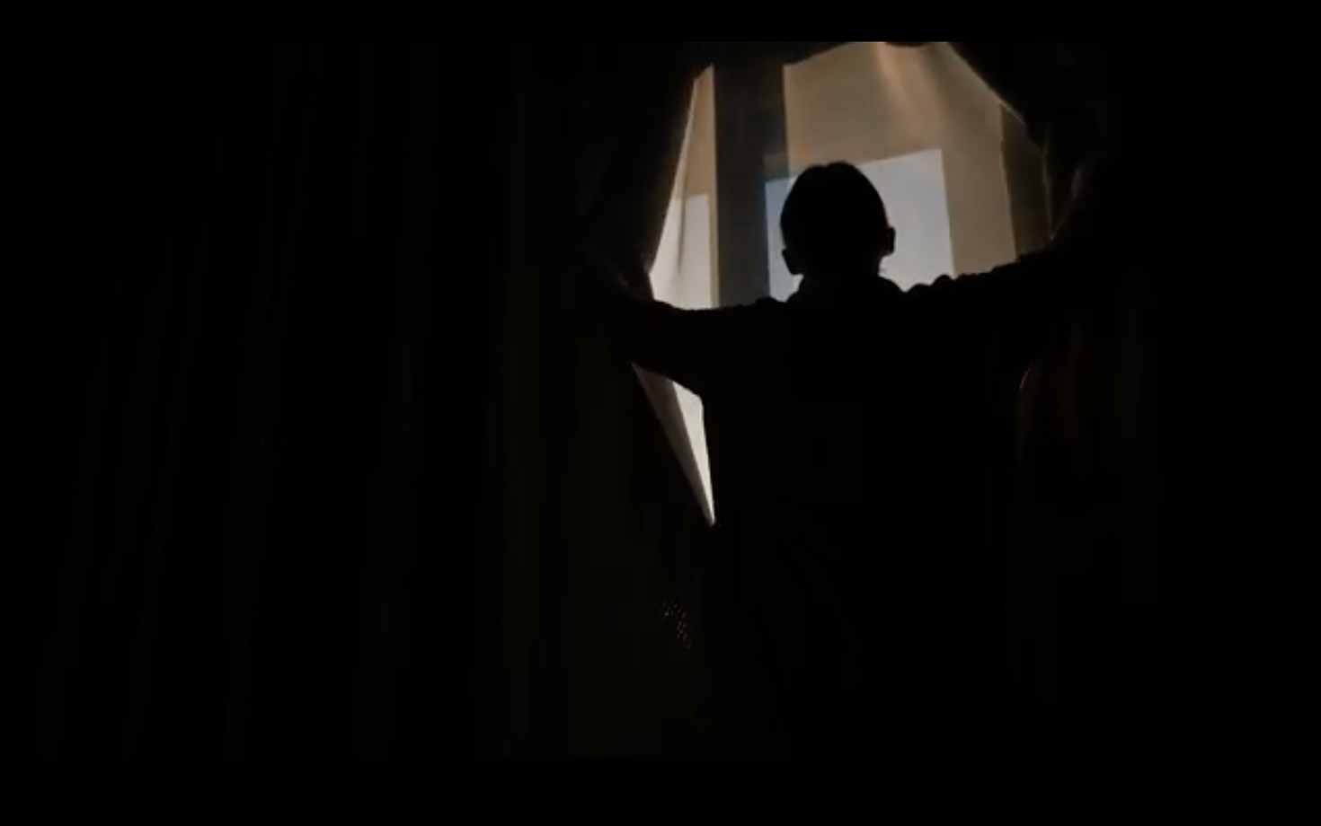 Schattenriss einer Person, die Vorhänge vor einem hell erleuchteten Fenster öffnet.