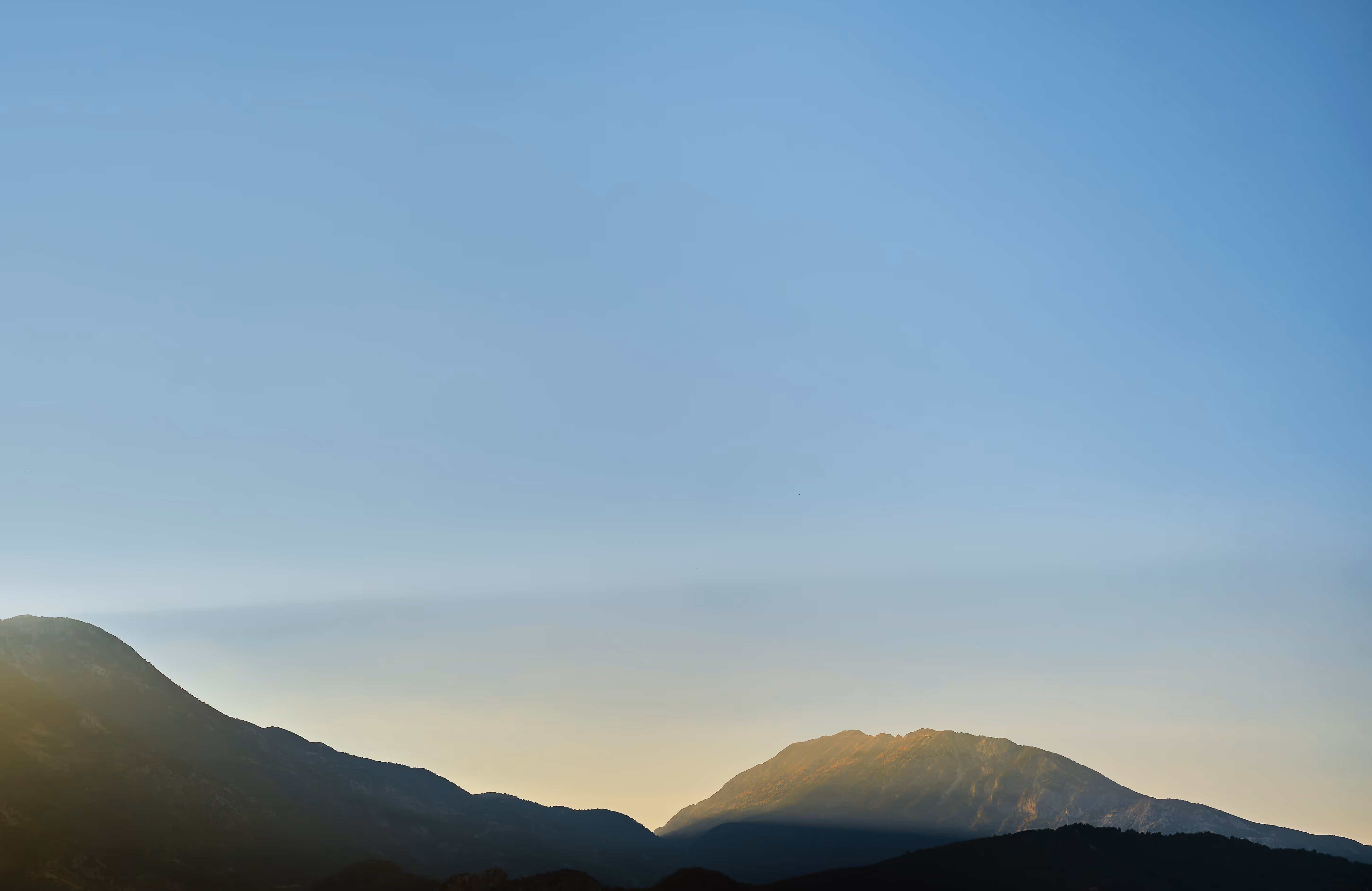 Berge im Gegenlicht mit klarem Himmel darüber bei Sonnenaufgang oder Sonnenuntergang.
