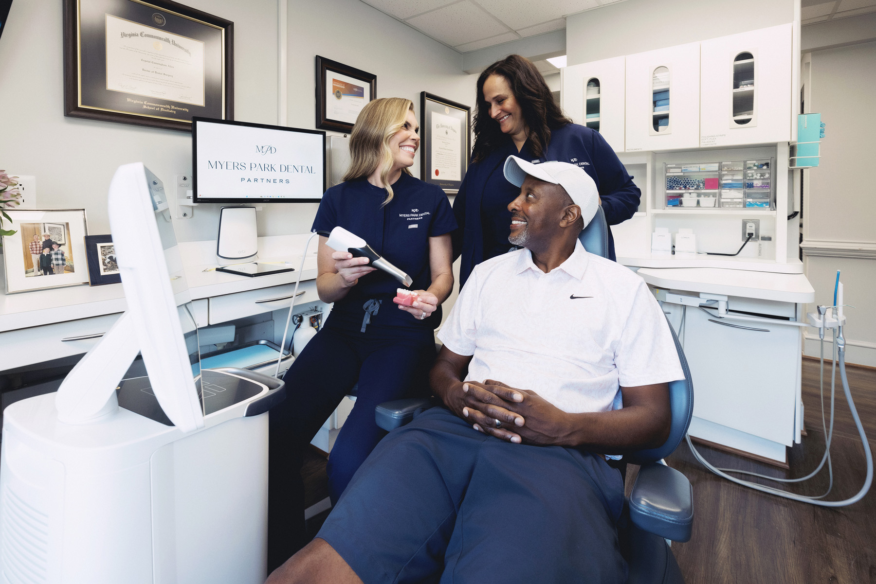 Two female dental professionals smiling and interacting with a male patient seated in a dental chair at Myers Park Dental.