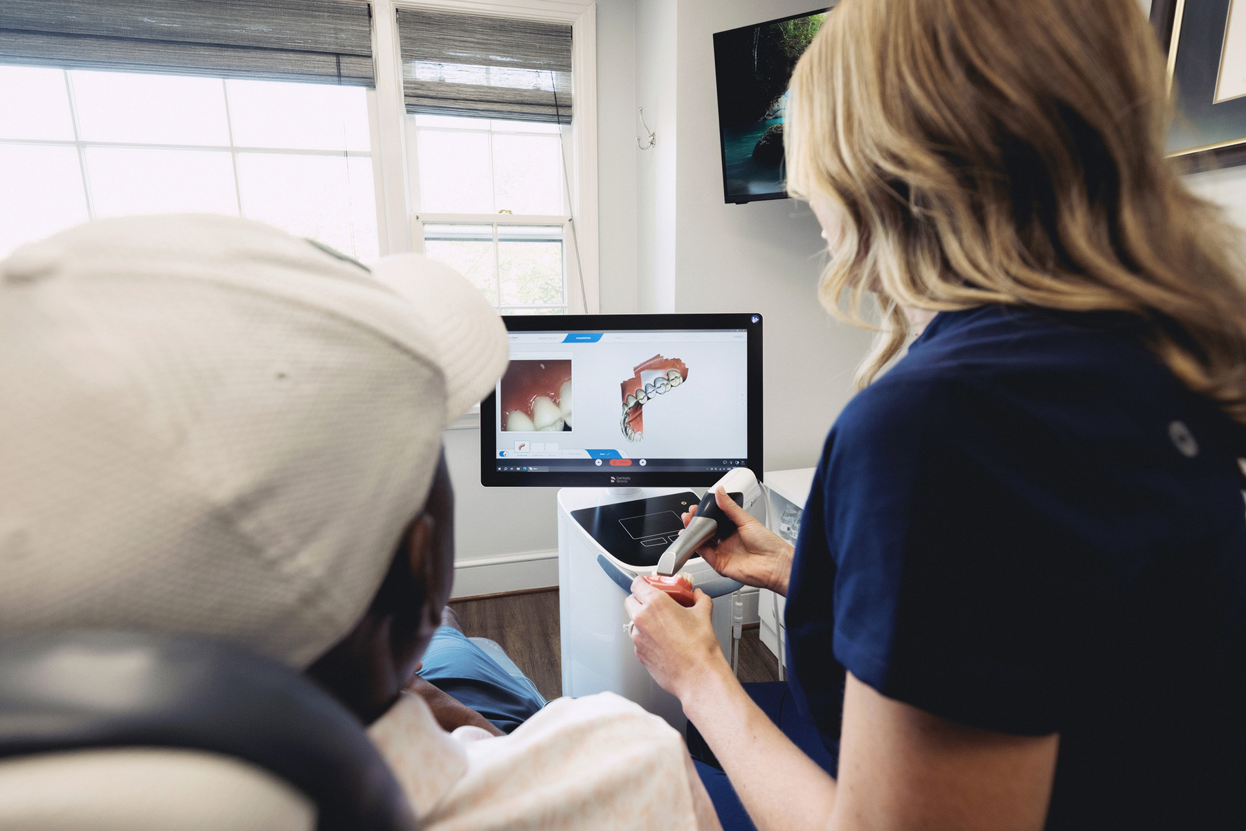 Dentist demonstrating dental imaging technology to patient using a 3D scanner and computer screen.