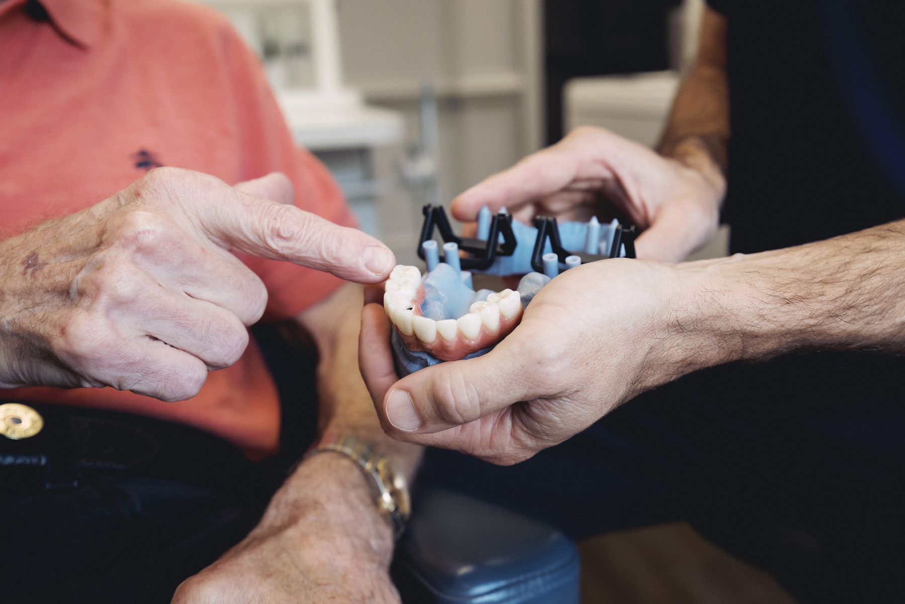 Close-up of a dental professional showing a dental model to an elderly person, who is pointing at it.