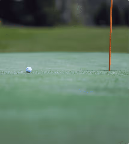 Golf ball on green grass near an orange flagstick on a golf course.