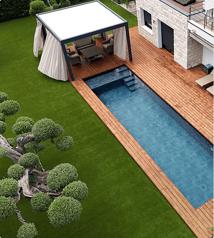 Modern outdoor patio with a white canopy, seating area, wooden deck, narrow rectangular pool, and green landscaped lawn.