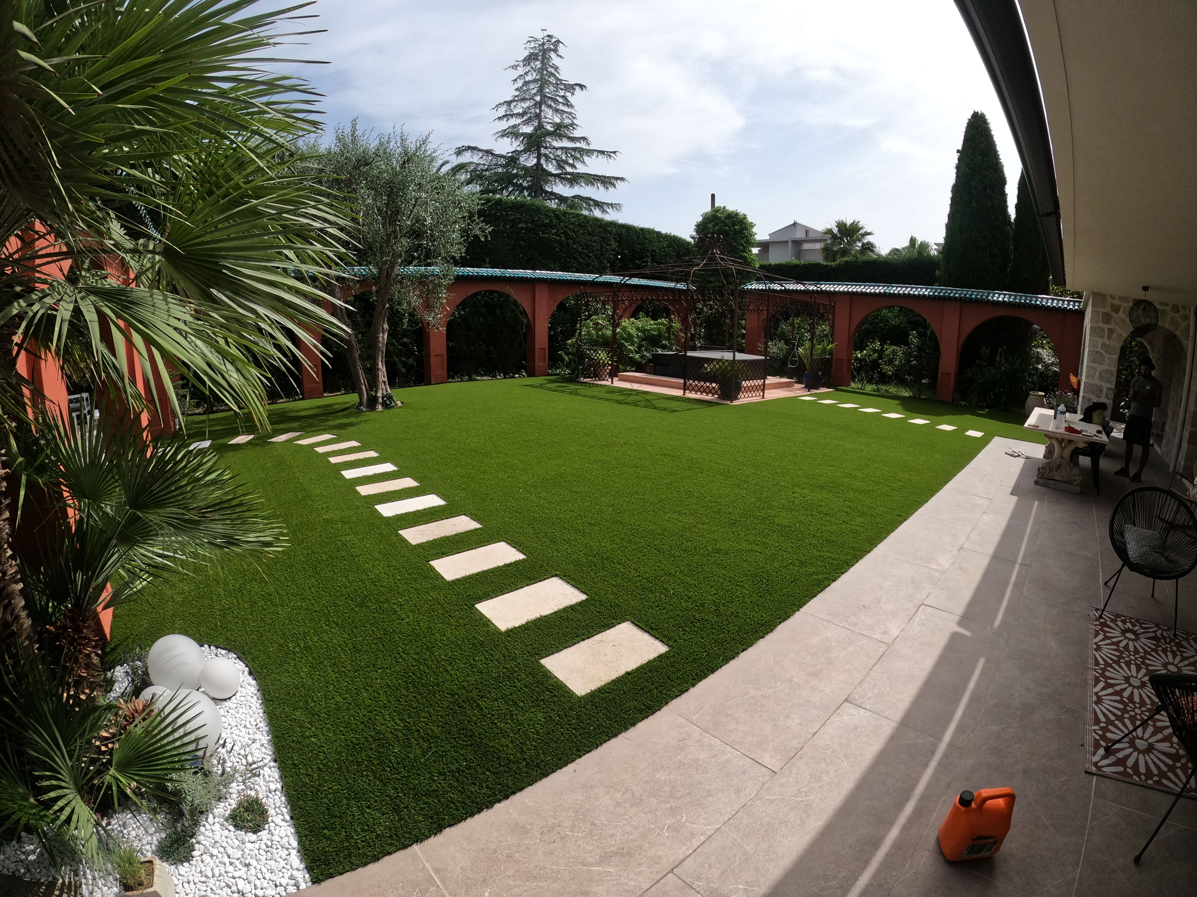 Well-maintained backyard with green grass, stone path, palm trees, and a pergola in the middle.