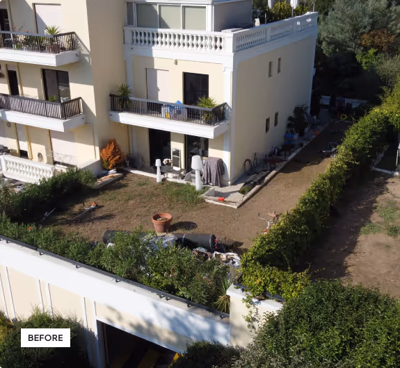 Backyard view of a residential building with a partly overgrown lawn, scattered garden items, and plants along the perimeter.