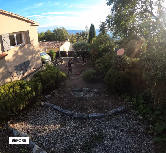 Garden area with bushes and gravel path next to a house, with a person working outdoors trimming or clearing vegetation under a bright, partly cloudy sky.