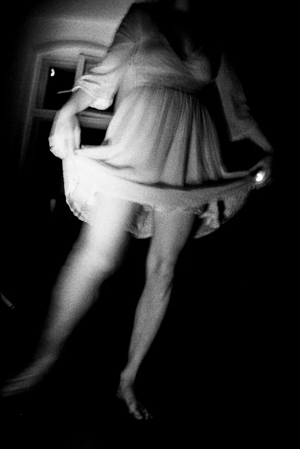 Black and white photo of a person in a dress holding its hem and lifting one leg forward.