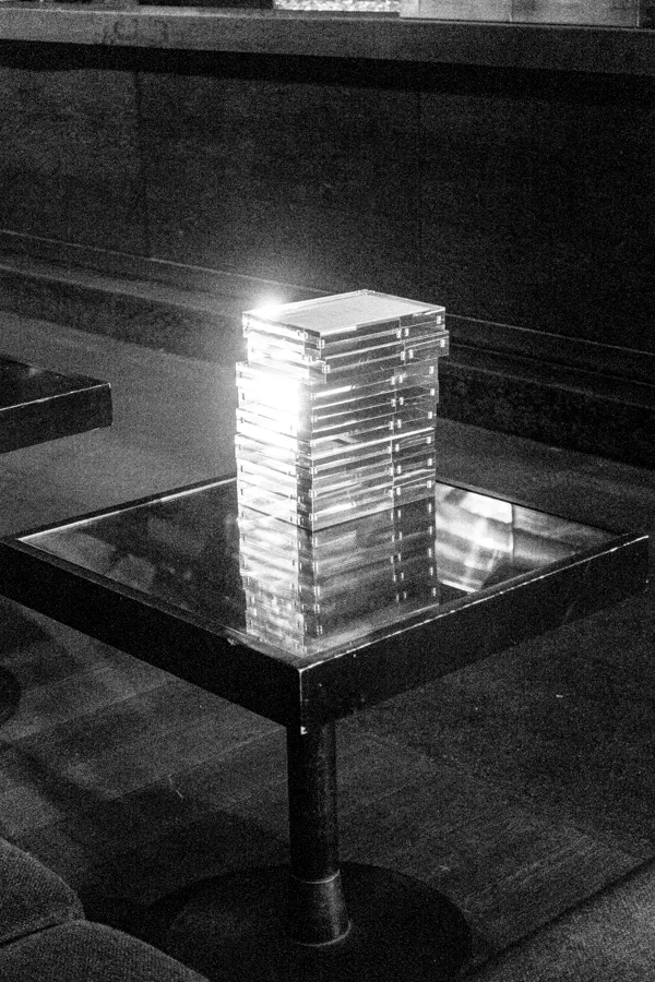 Stack of clear plastic CD jewel cases on a reflective square table inside a dimly lit room.