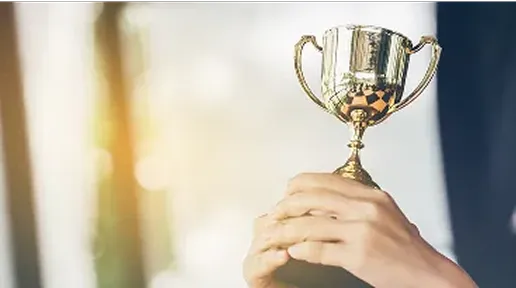 Person holding up a gold trophy cup with both hands against a blurred background.