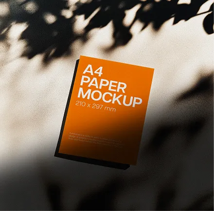 Orange A4 paper mockup with shadows of leaves on a light surface.