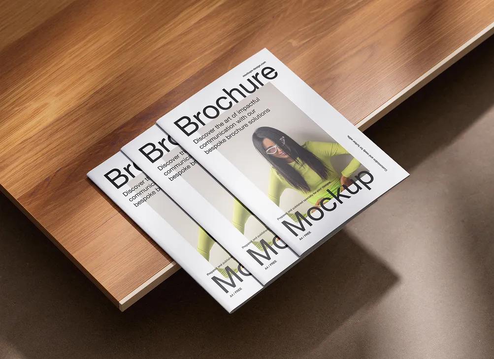 Three brochures stacked on a wooden table displaying a design with a woman in glasses wearing a yellow-green top and text reading 'Brochure Mockup'.