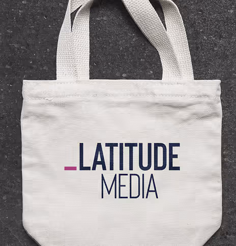 Canvas tote bag with Latitude Media logo on dark textured surface.