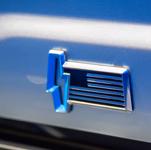 Close-up of blue electric vehicle emblem on metallic car surface.