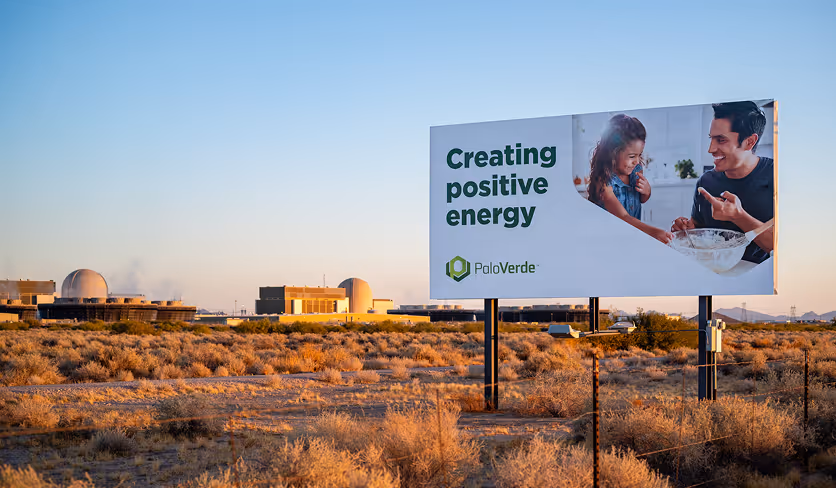 Billboard displaying Palo Verde message “Creating positive energy” in desert landscape near power plant.