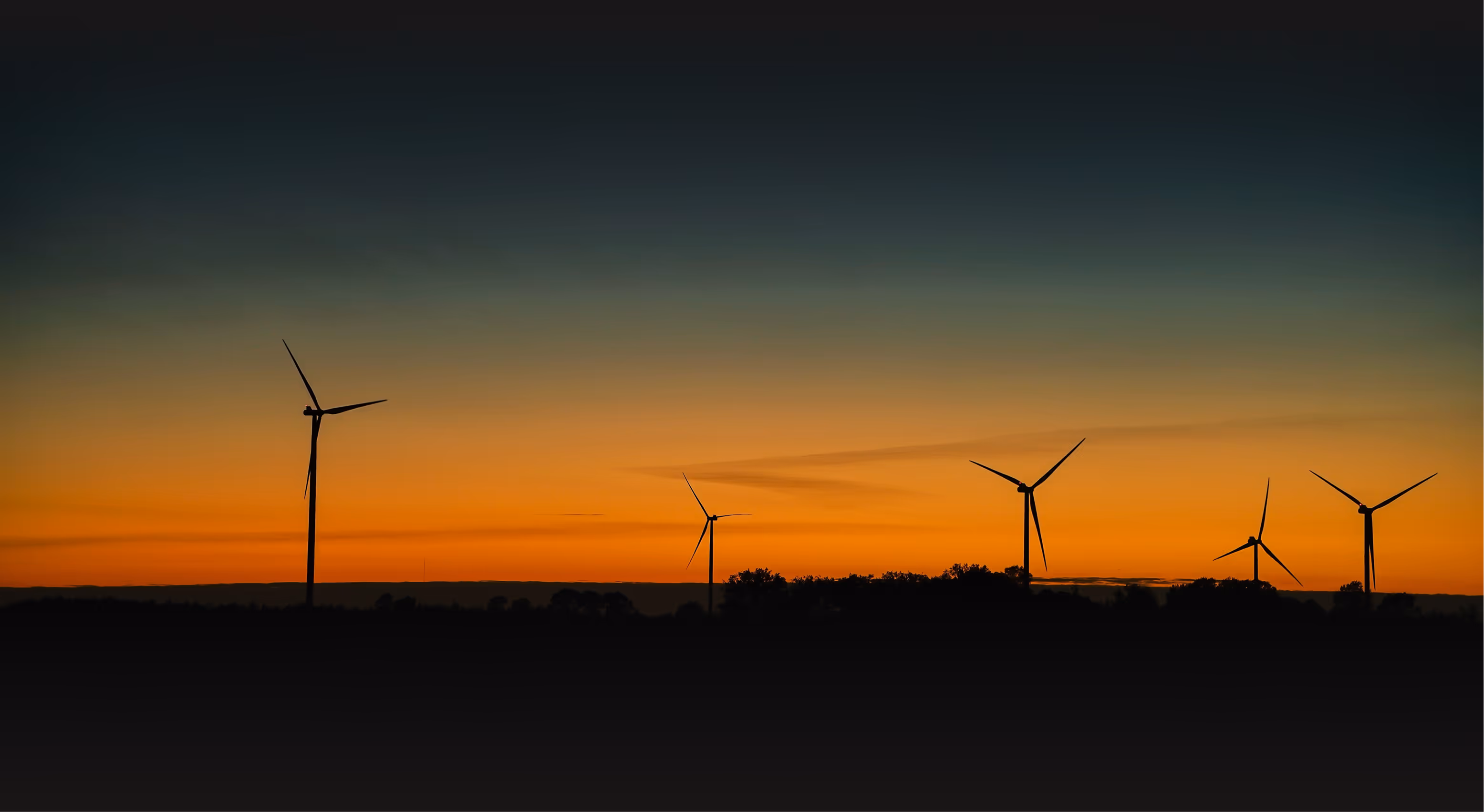 Wind turbines silhouetted against an orange sunset sky, symbolizing clean renewable energy and sustainable power generation.