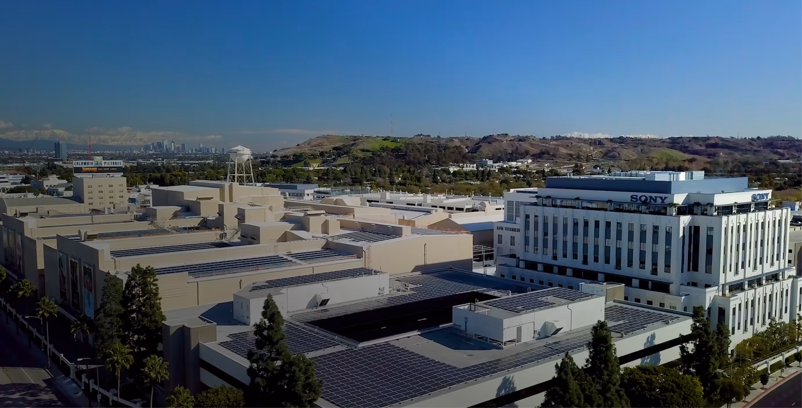 Aerial view of the Sony Pictures Studios complex with solar panels on the rooftops and hills in the background under a clear blue sky.