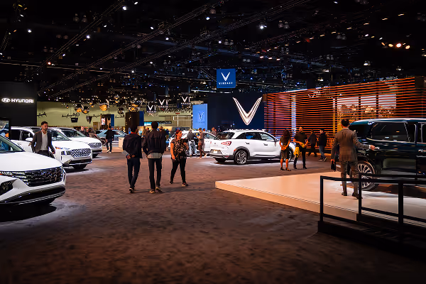 People walking through a modern auto and energy expo showcasing electric vehicles and clean technology — representing DG+’s deep experience working with over 100 clean energy and climate organizations worldwide.