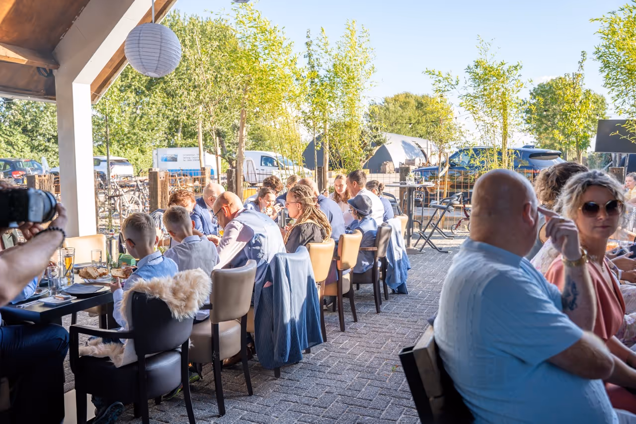 Group of people seated outdoors at a long table enjoying a meal and conversation on a sunny day.