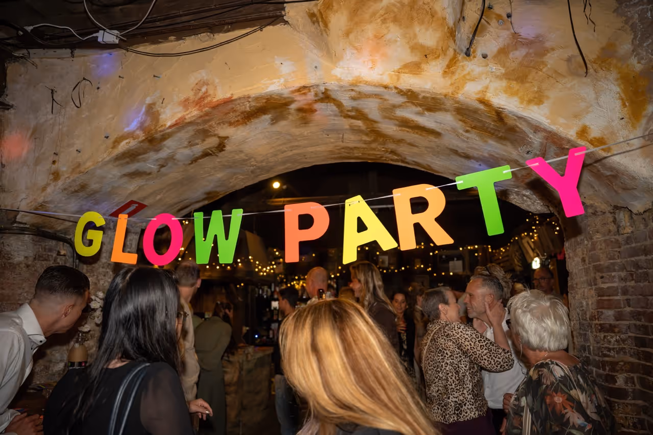 Group of people socializing under a stone archway with colorful 'GLOW PARTY' letters hanging above.