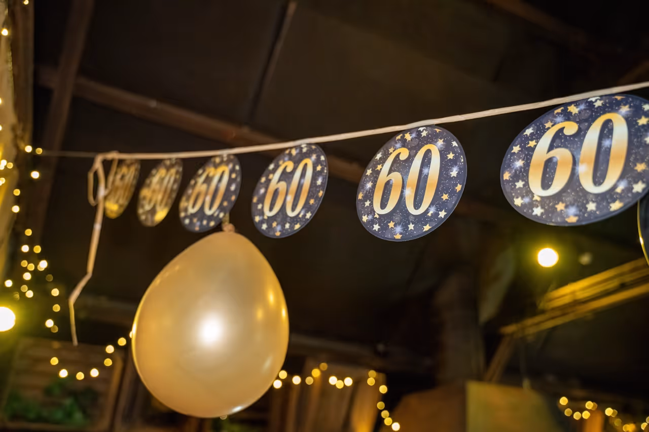 String of circular decorations with the number 60 and stars, hanging with a gold balloon and warm fairy lights in the background.