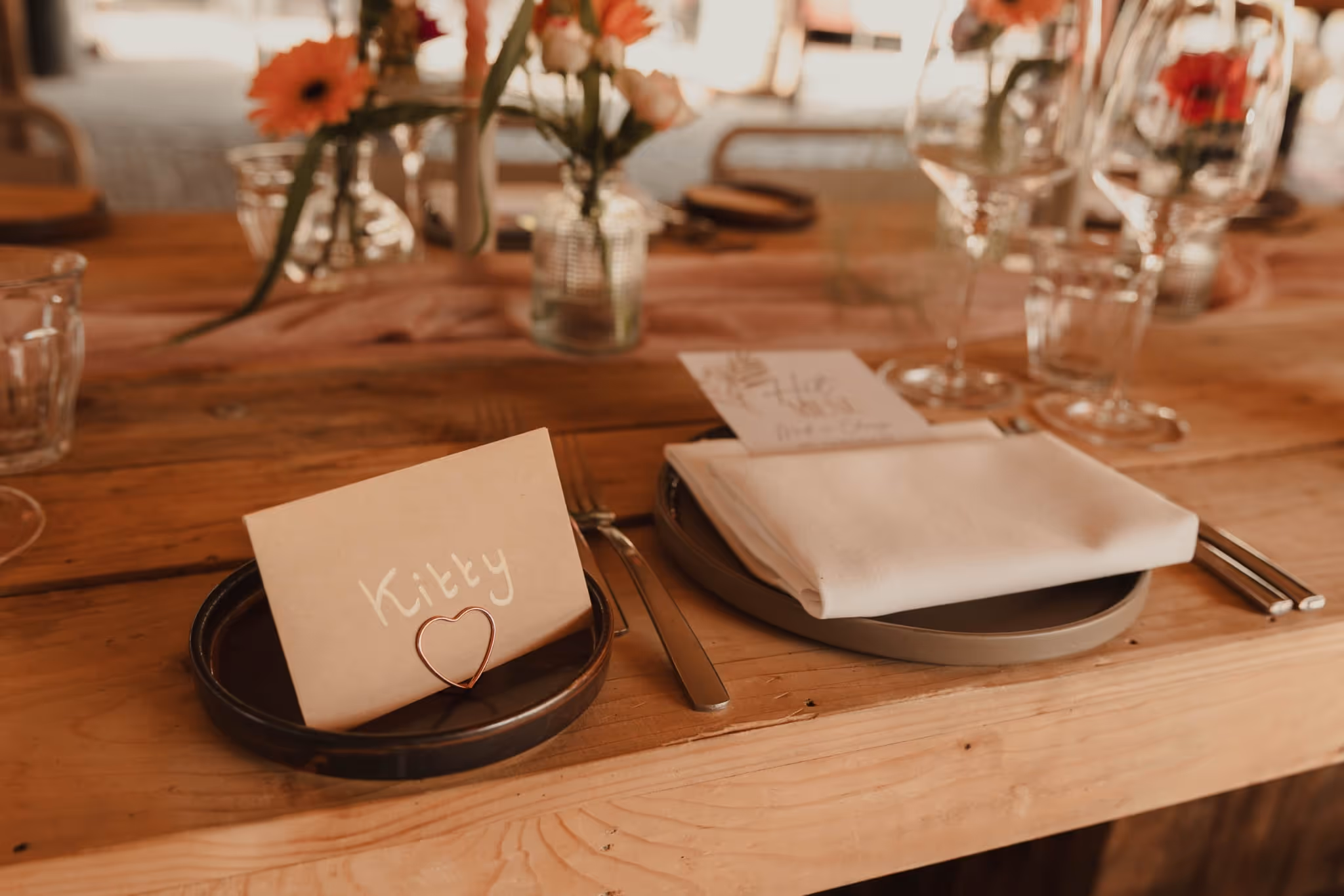 Rustic wooden table set with plates, fork, knife, folded white napkin, and a name card holder with ‘Kitty’ written on the card.