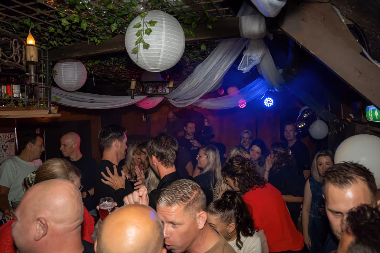 Groep mensen die in een gezellige, gedimde ruimte met witte lampionnen en lichte decoraties samenkomen en socializen.