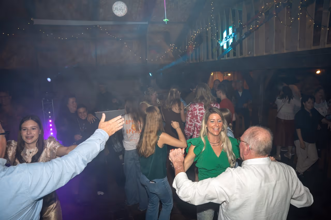Groep mensen danst en viert feest in een sfeervolle ruimte met dimlicht en feestverlichting.